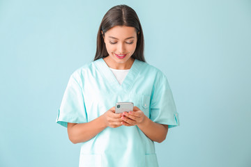 Young nurse with mobile phone on color background