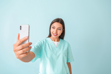 Young nurse taking selfie on color background