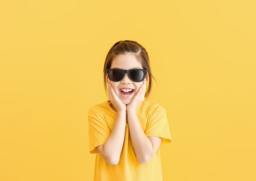 Funny little girl with sunglasses on color background