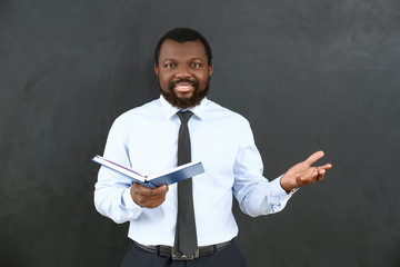 African-American teacher with book near blackboard in classroom