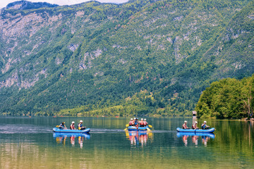 Scenery with people canoeing on Bohinj Lake in Slovenia. Nature and men kayaking on water in Slovenija. Beautiful landscape view in summer. Alpine Travel destination. Julian Alps mountains