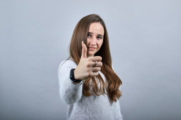 Cheerful caucasian lady keeping thumbs up, smiling wearing fashion blue sweater isolated on gray...
