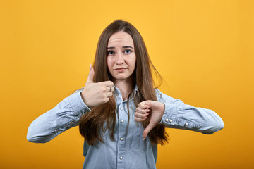 Attractive caucasian lady wearing fashion shirt isolated on orange background in studio keeping thumbs up and down, looking at camera. People emotions, lifestyle concept.