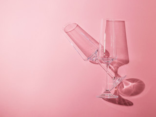 Two crystal glasses on long legs on a pink background.