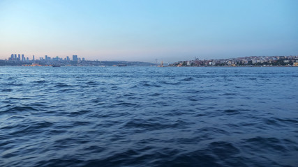 calm deep blue sea waves against distant famous city buildings under blue purple sky in dusk view from sailing ship