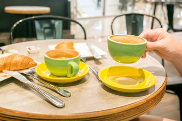 Coffee and croissants in cafe, hands of woman closeup. Breakfast in caffeine.