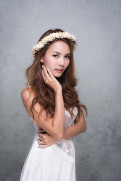 Vintage style portrait beautiful woman wearing a white dress, flower crown on gray soft blurred background.