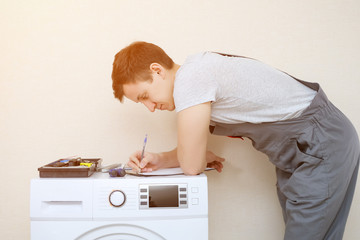 man with set of tools writes on clipboard examining modern washing machine with screen on control panel in room