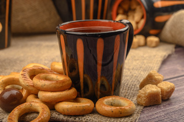 Small bagels, chocolates, a mug of tea and a rough homespun cloth on a wooden background close-up.