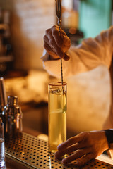 Bartender stirring a cocktail in a highball glass with crystal clear ice inside, at the bar counter. Selective focus, lifestyle vertical photo