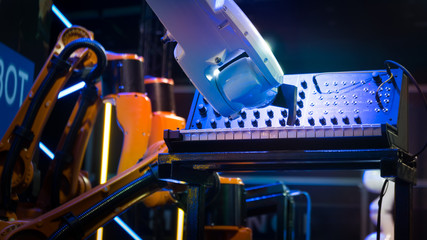 Futuristic look industrial robotic arm and hand plays electric piano with sound synthesizer with other robots operating various musical instruments. All are ai, automated and programmable.