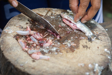 A woman is cutting the belly the fish and taking away the intestines,  Which may have parasites in it, than washing by clean water and cooking in the next order