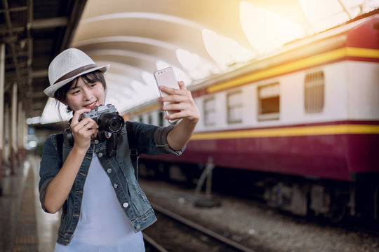 Side view of young woman smile, tourist girl with backpack taking photo of train station landscape view and smile happily. at the railway station, Backpacker concept, vintage train,blurred background