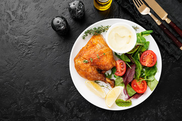 Baked chicken leg, served with sauce and fresh green salad. Black background