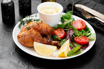 Baked chicken leg, served with sauce and fresh green salad. Black background
