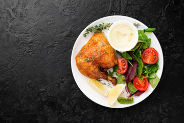 Baked chicken leg, served with sauce and fresh green salad. Black background