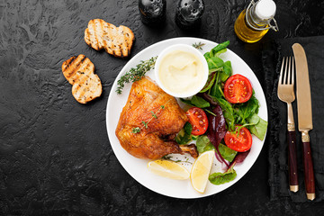 Baked chicken leg, served with sauce and fresh green salad. Black background