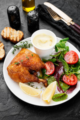 Baked chicken leg, served with sauce and fresh green salad. Black background