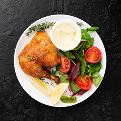 Baked chicken leg, served with sauce and fresh green salad. Black background