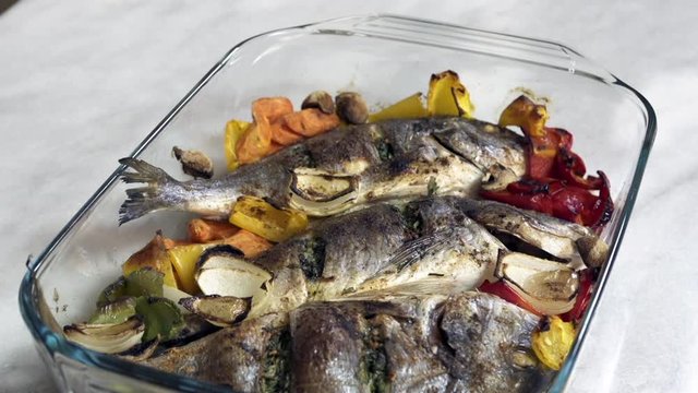 Putting roasted sea bream fish with with vegetable on table