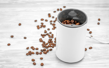 Close-up electric coffee grinder with coffee grains scattered around on a wooden table.