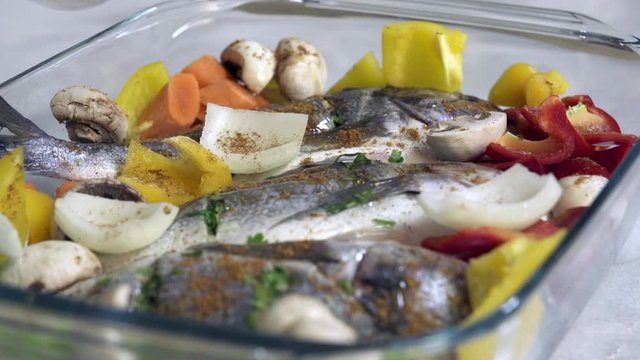 Pouring oil on fresh sea bream fish with with vegetables just before roasting in oven
