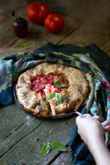 Rustic tomato galette on dark wooden table  sprinkled with fresh basil and sesame seeds cut in one slice