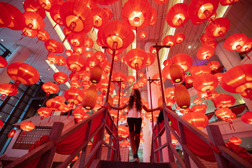 Woman walking and enjoying traditional red lanterns decorated for Chinese new year Chunjie. Asian culture inspiration. Trend lava color. - obrazy, fototapety, plakaty