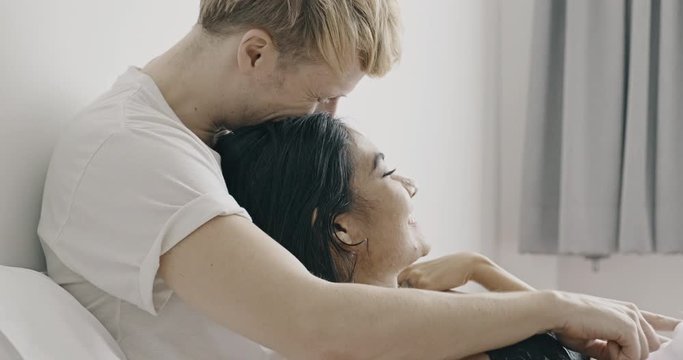 Lover sitting in bed talking and laugh. Caucasian male with his girlfriend, asian woman in black lingerie. Happy lover in bed concept.