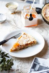 Slice of Quince and almond tart sprinkled with powdered sugar on a rustic white table with a can of jam in background.
