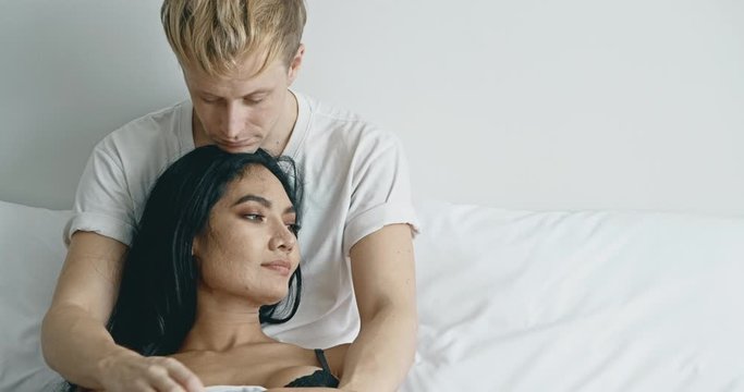 Lover sitting in bed thinking about future. Caucasian male with his girlfriend, asian woman in black lingerie. Happy lover in bed concept.
