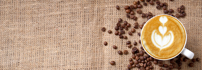 Cup of coffee latte art and coffee beans on jute long panoramic with space for text