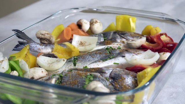 Sprinkle spices on fresh sea bream fish with vegetables just before roasting in oven