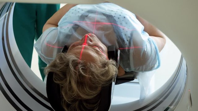 Close-up shot of a female mature patient lying on a table of CT scan machine. Computer tomograph scanning brain of elderly woman. High-tech equipment in medical clinic. 4K