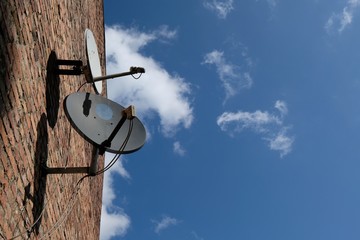 Satellite dish plates on a red brick wall of old house against a blue sky.
