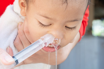 .Mother is injecting the saline solution from Syringe into the nose of the boy to wash the mucus.