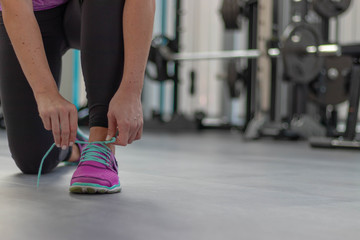 Fototapeta na wymiar Frau in Sportbekleidung schnürt Sportschuhe auf dem dunklen Boden eines Fitnessstudios mit Gewichten