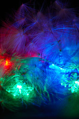 Obraz na płótnie Canvas A fragment of a luminous multi-colored Christmas garland and natural fluff on a black background