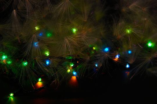 A fragment of a luminous multi-colored Christmas garland and natural fluff on a black background