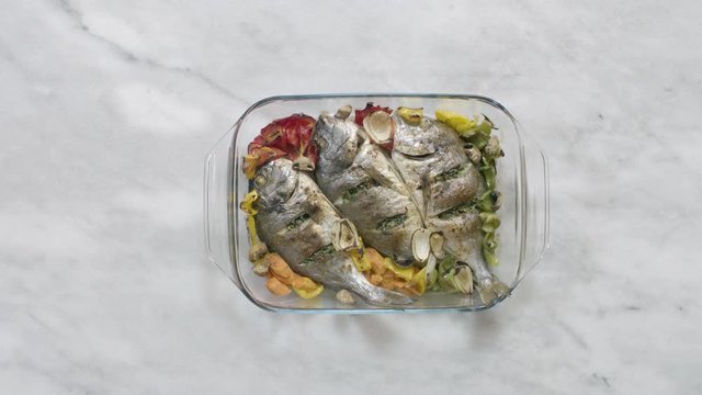 Putting roasted sea bream fish with vegetable on table, top view