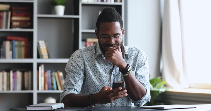 Happy young adult african man using smartphone in home office