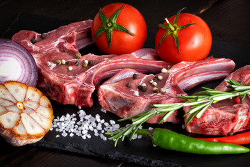 Raw meat mutton lamb ribs with herbs on black stone background with spices and fresh vegetables