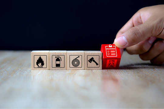 Close-up hand choose a red wooden toy blocks with insurance policy icon for fire safety protection concepts.