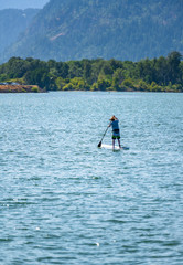 Naklejka premium A man in a hat floats on the river standing with an oar on an inflatable board