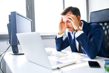 Shot of mature businessman suffering headache, flu in office