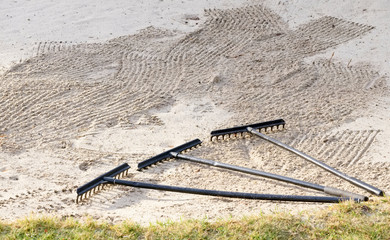 Rake in sand bunker at golf links course green for golfers