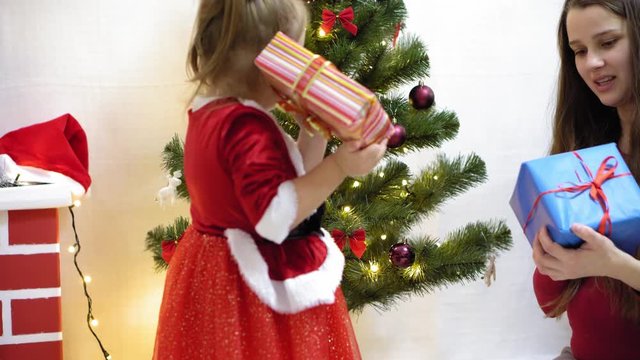 baby and pregnan mom hang red ball toy on Christmas tree. happy childhood concept. child and mother decorate tree with christmas balls. small child and a parent are playing by Christmas tree.