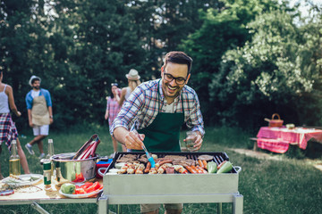 Handsome male preparing barbecue outdoors for friends - obrazy, fototapety, plakaty