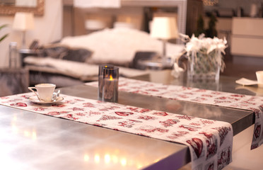 A tablecloth with Christmas pattern on a designers table with modern candles and a coffee cup on it in luxury blurred  interior
