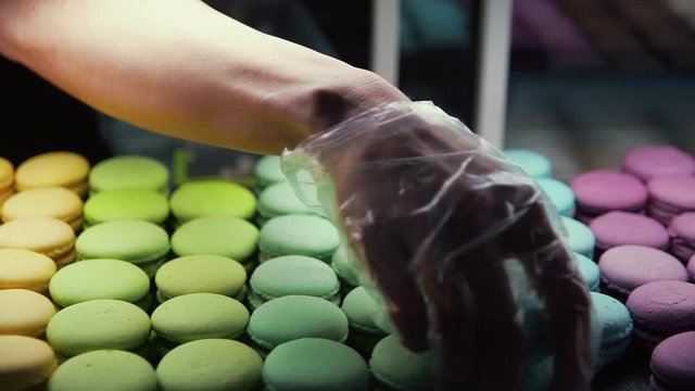 Closeup chef hand putting macarons at showcase. Colorful macarons at store glass
